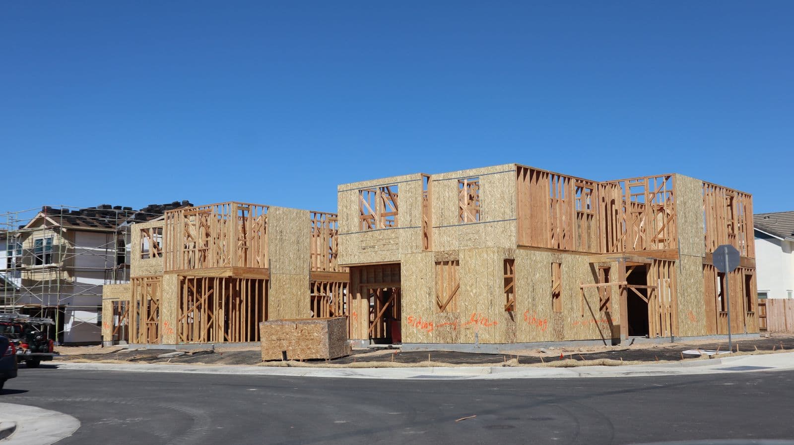A new house under framing against a clear blue sky, on a street of homes under construction