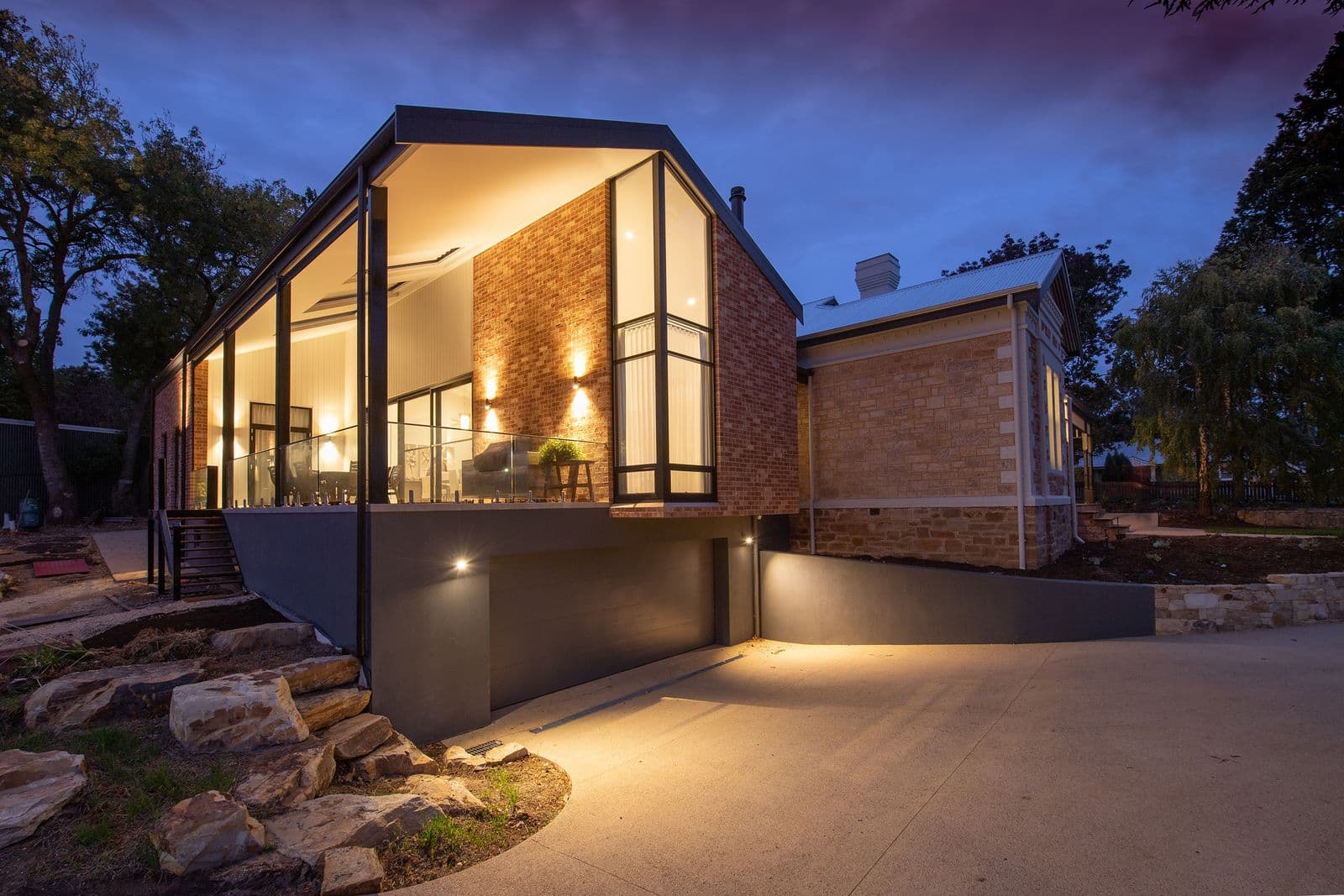 A modern brick home lit from within at dusk, under a deep blue and purple sky