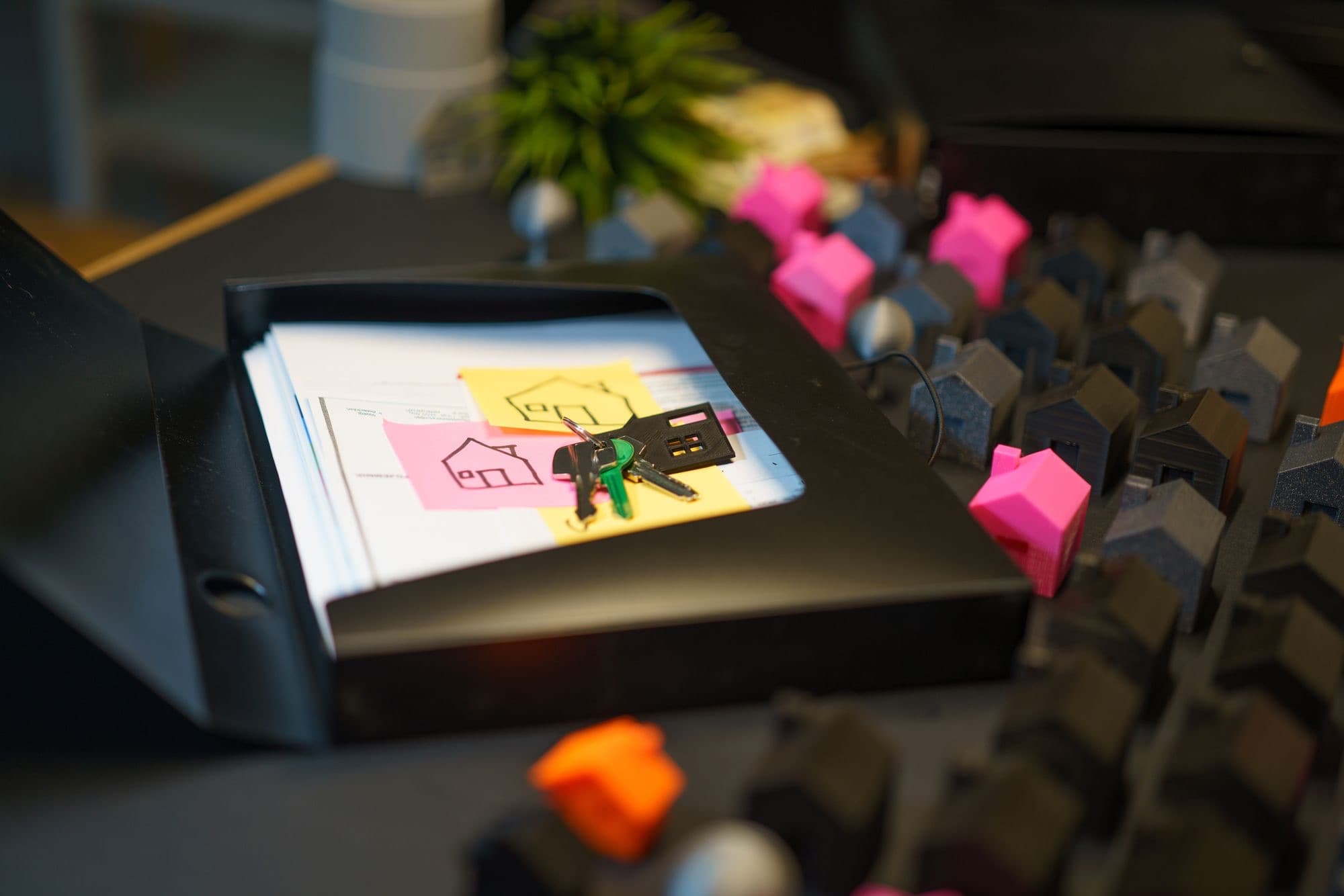 A set of house keys on a document folder, with house-shaped sticky notes and small model houses beside it