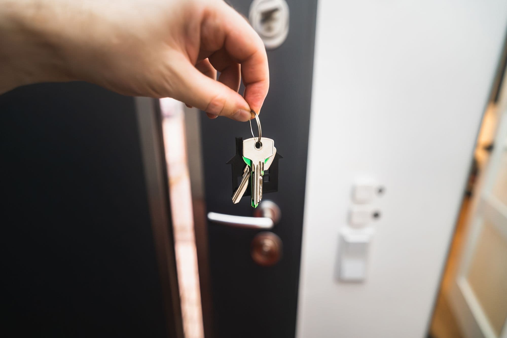 A close-up of a hand holding a set of house keys in front of an open front door