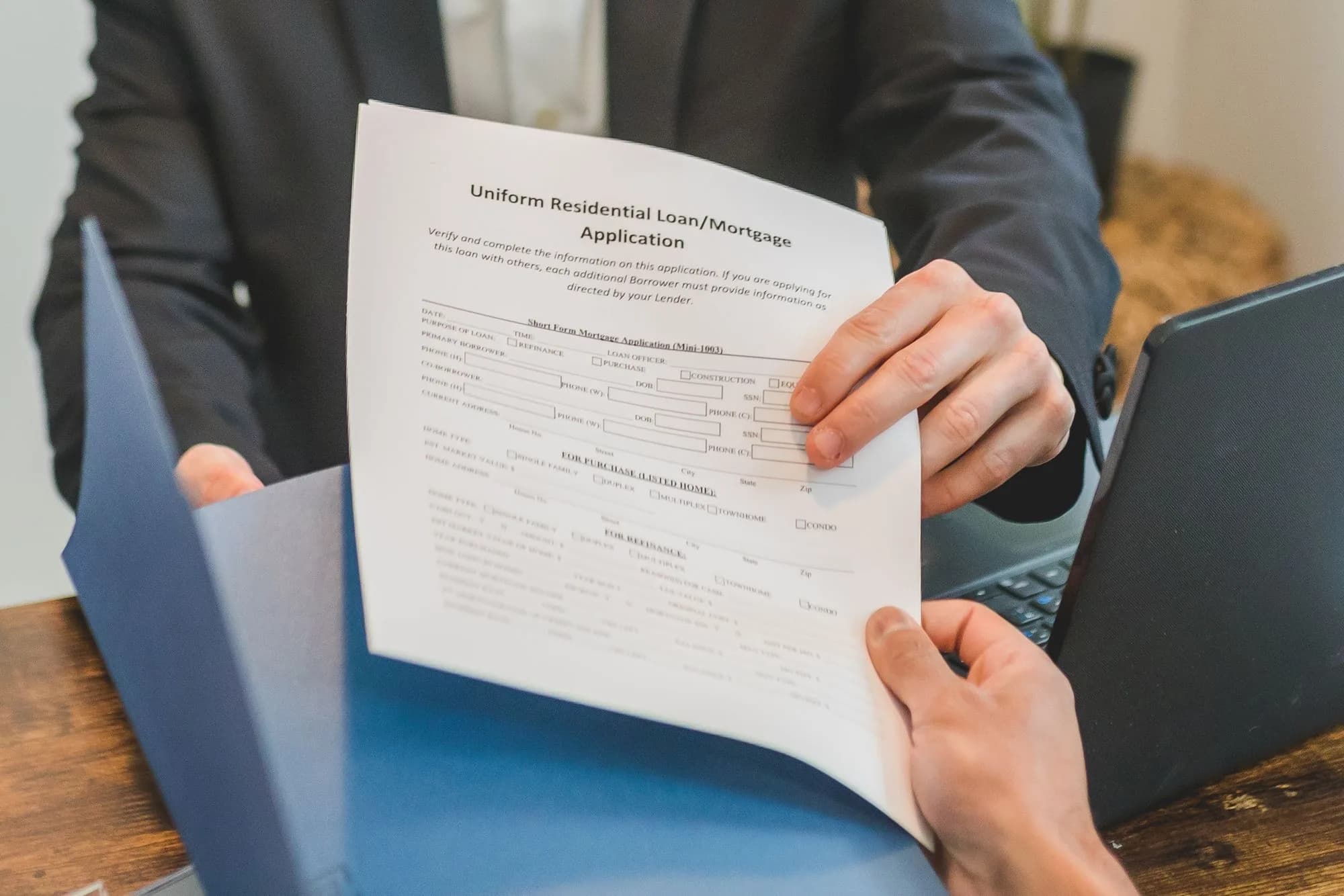 A lender across a wooden desk handing over a blank mortgage application in a folder