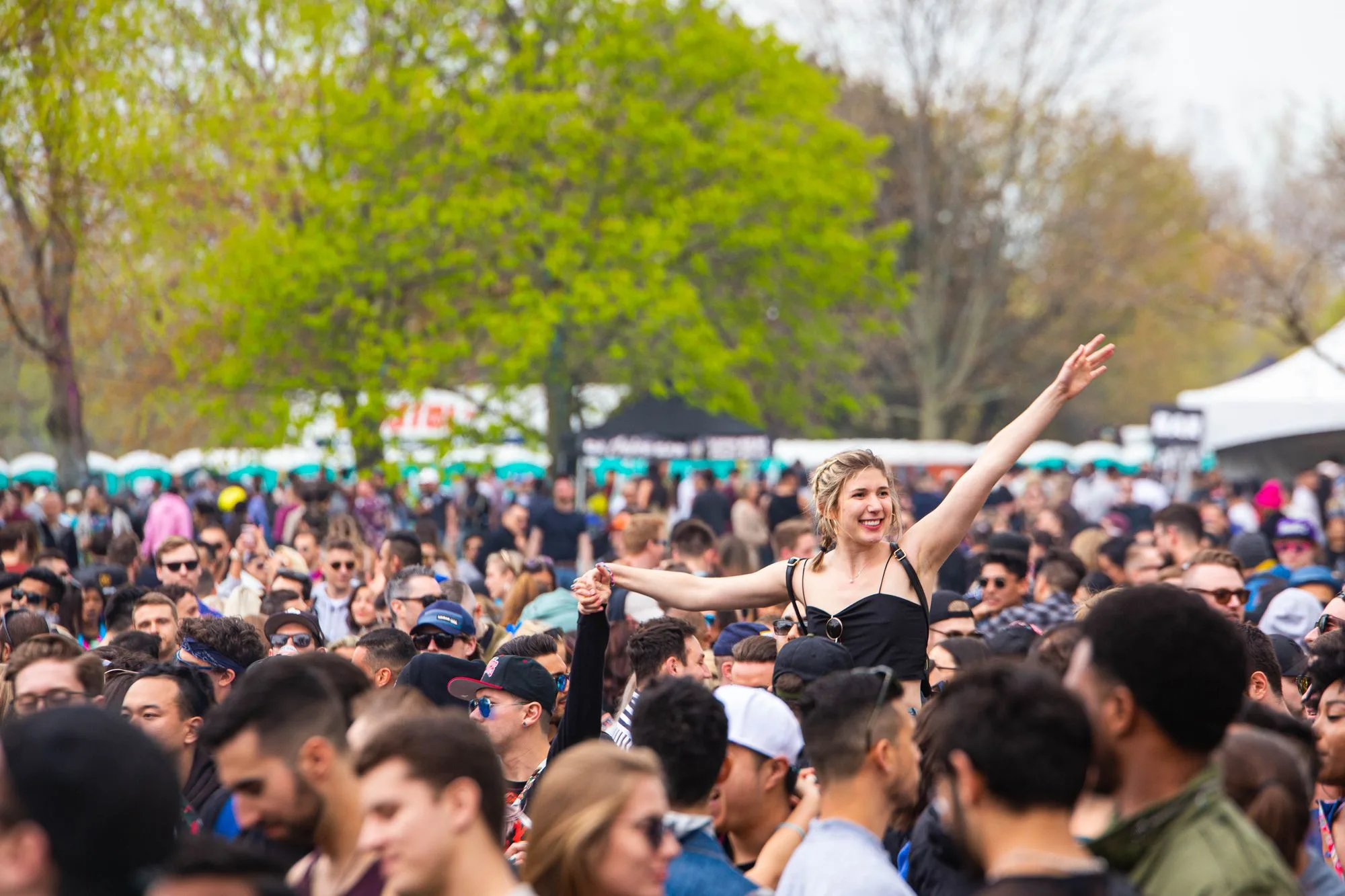 A daytime outdoor music festival crowd under spring trees