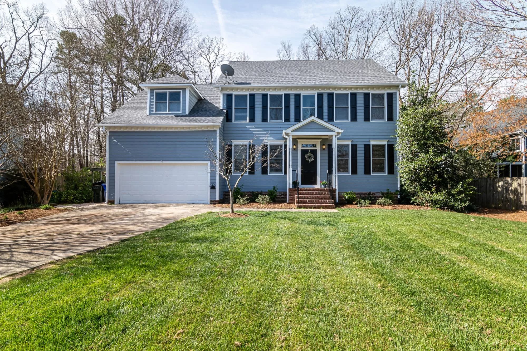 A well-kept two-storey colonial house with a two-car garage and a wide front lawn
