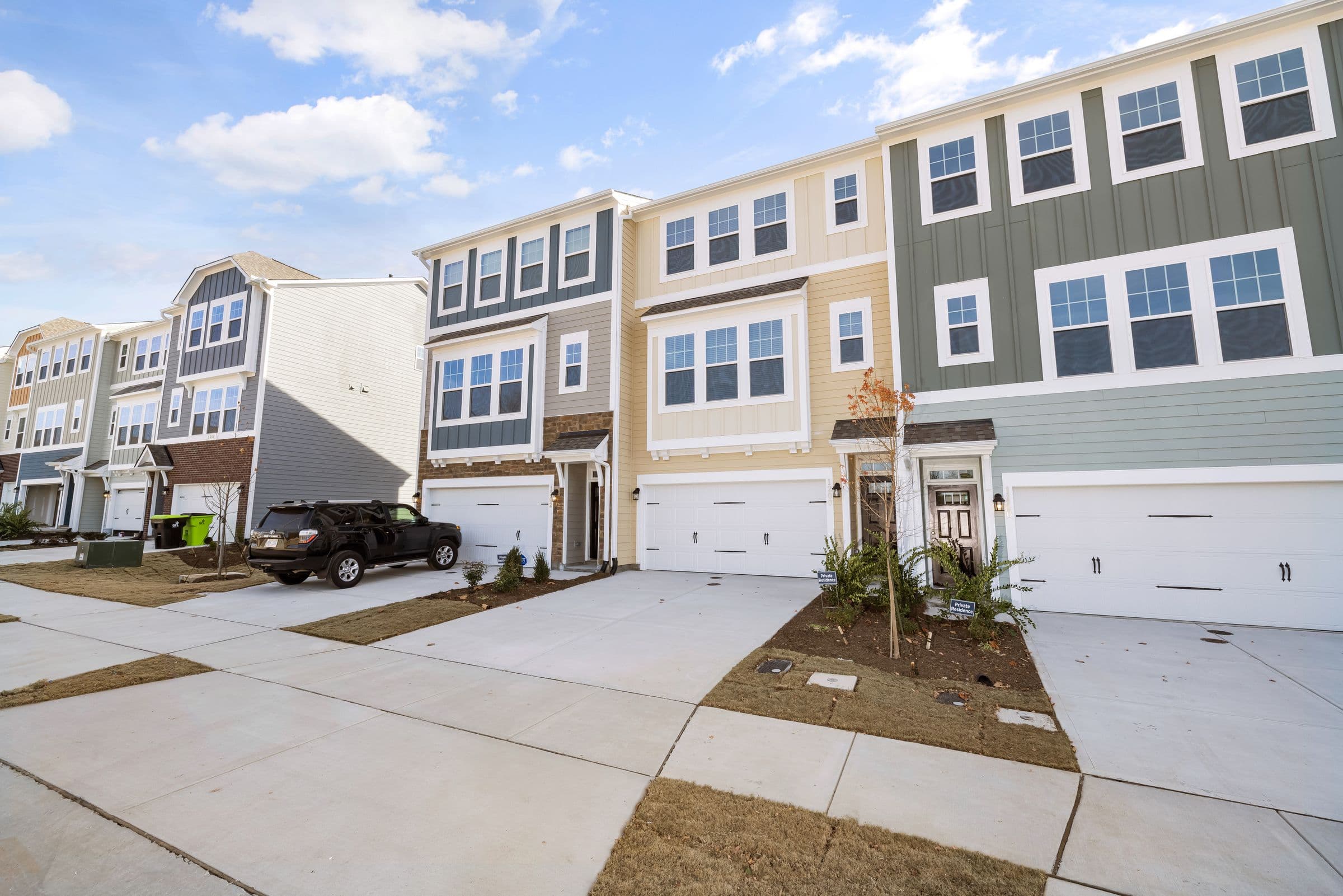 A row of newly built townhomes with fresh sod, new driveways and white garage doors under a blue sky