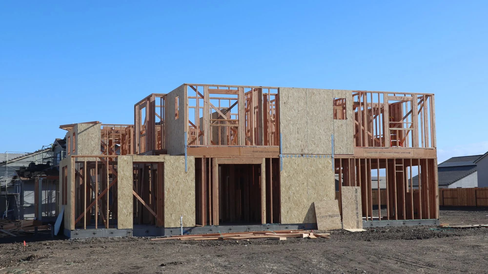 A two-storey house under framing on a bare lot between finished homes