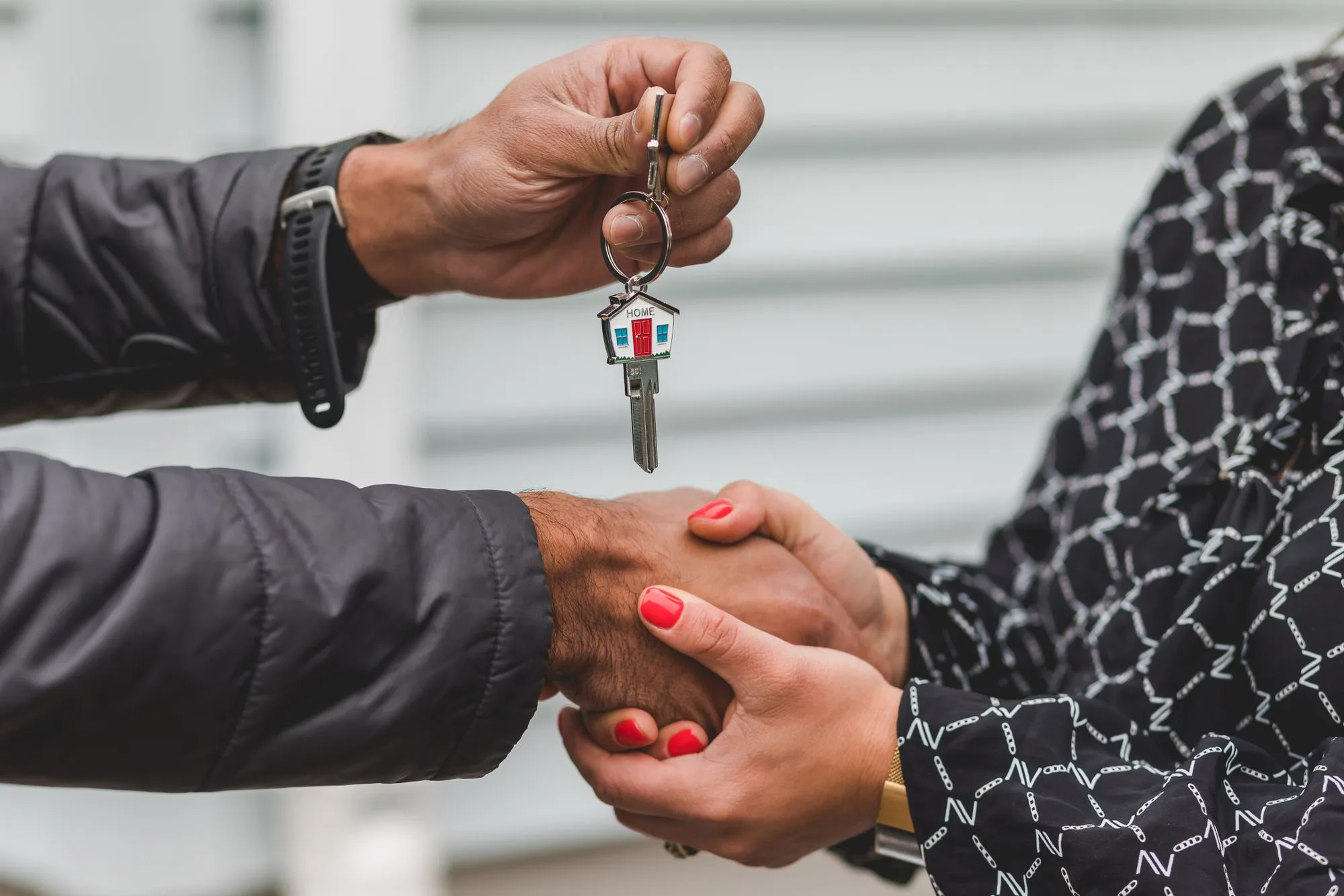 A handshake outside a house, one hand holding a key on a house-shaped fob